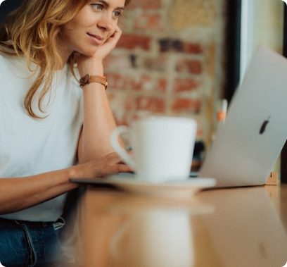 A woman browsing on her laptop with a mug on her side